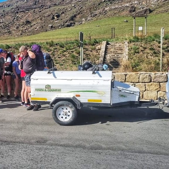 Hiking group loading packs onto the white luggage trailer at a mountain trailhead