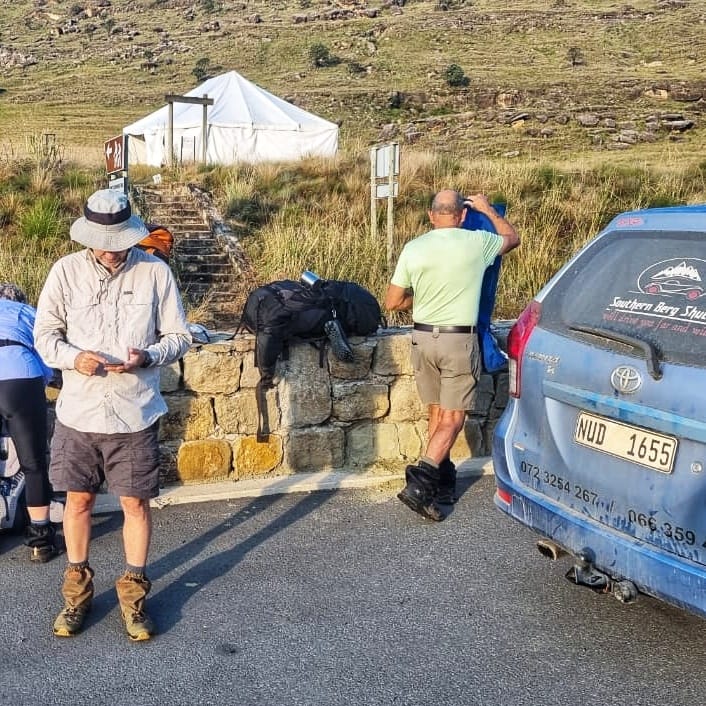 Hikers checking their route beside the branded Southern Berg Shuttle vehicle at a Drakensberg trailhead