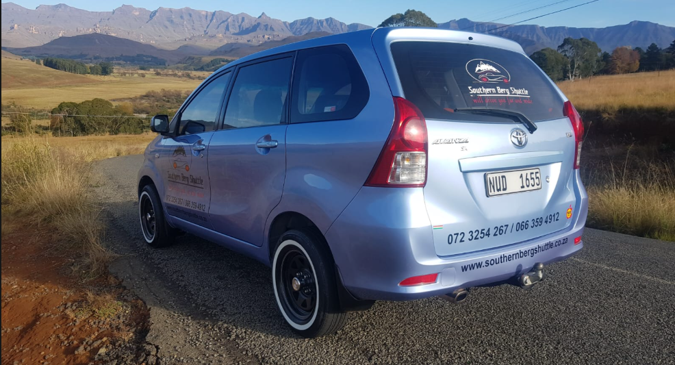 Southern Berg Shuttle Toyota Avanza on a gravel road with the Drakensberg peaks behind