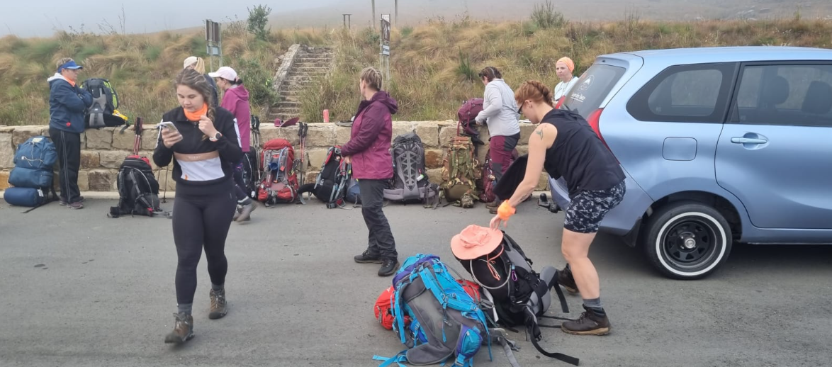 Hikers sorting backpacks beside the shuttle on a misty morning start